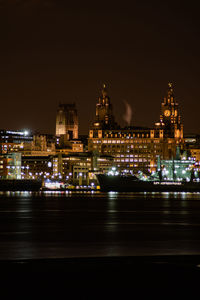 Illuminated city by sea against sky at night