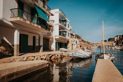 Sailboats moored on sea by buildings against blue sky