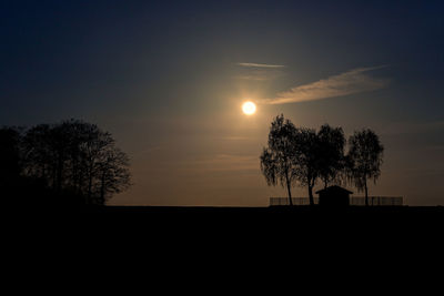 Silhouette trees on field against sky at sunset