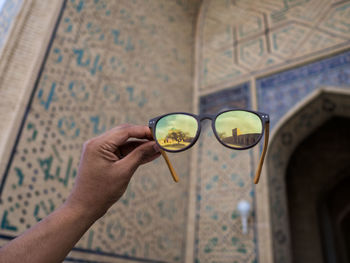 Cropped hand holding sunglasses against building