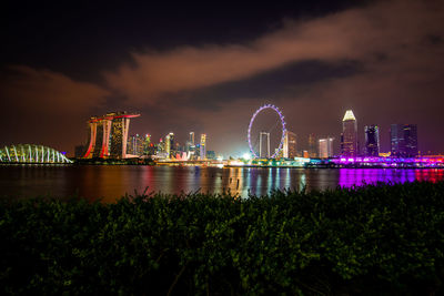 Illuminated city by river against sky