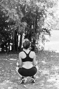 Rear view of teenage girl crouching while exercising on field against trees in park