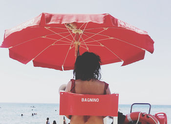 Rear view of woman with umbrella on beach against sky