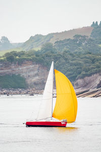 Sailboat sailing on sea against mountain