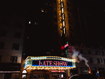 Low angle view of illuminated text on street in city at night