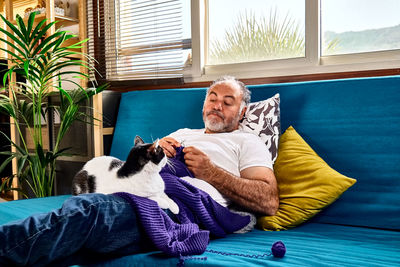 Bearded man plays with his cat while knitting as part of his hobby to keep a positive mental health