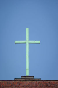 Low angle view of cross on building against clear blue sky