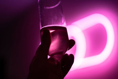 Close-up of hand holding glass against pink light 