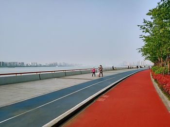 People walking on road by sea against clear sky