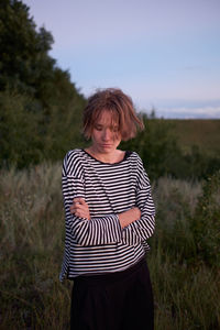 Thoughtful woman with arms crossed standing on land against sky