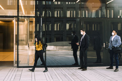 Business people with face masks standing in line outside office building