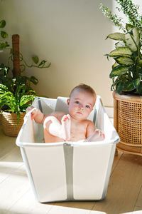 Little baby bathing in brightly lit room among flowers showing his bare feet