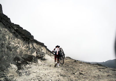 Man riding bicycle on mountain against clear sky