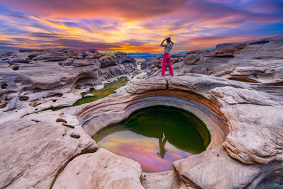 Rear view of woman standing on rock against sky during sunset