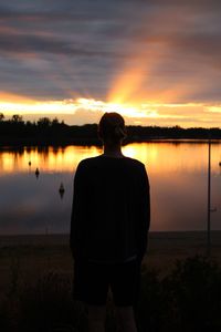 Rear view of silhouette man standing by lake against sky during sunset