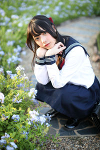 Full length portrait of woman crouching by flowering plants