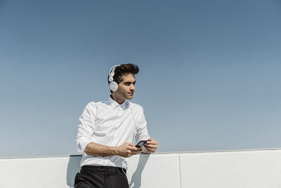 Low angle view of man using mobile phone against clear sky