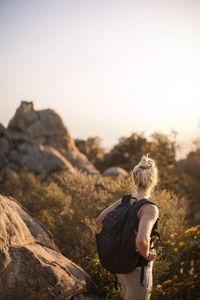 Woman carrying backpack while hiking in forest against clear sky