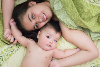 Portrait of shirtless woman with son lying on bed at home