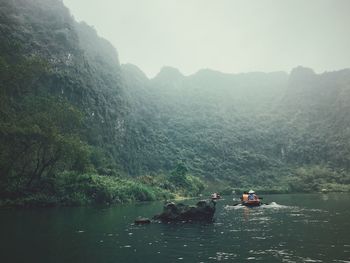 People boating on river amidst mountains against sky
