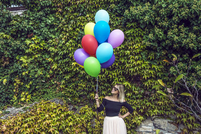 Woman with colorful balloons against wall