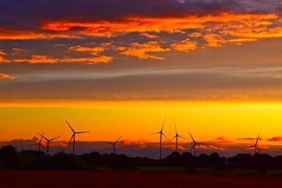 Silhouette wind turbines on field against orange sky
