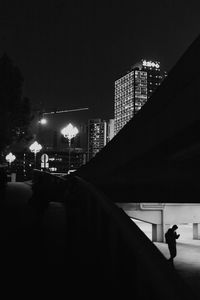 Man walking on illuminated street amidst buildings in city at night