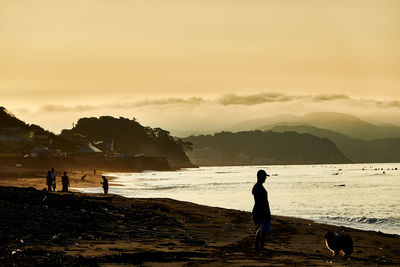 Silhouette people on beach against sky during sunrise