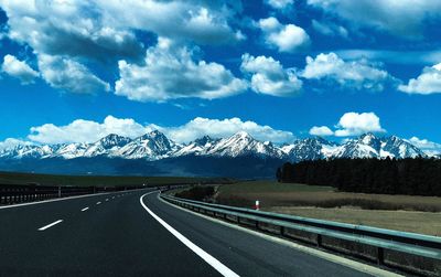 Empty road leading towards mountains against cloudy sky