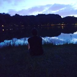 Rear view of man sitting at lakeshore against sky