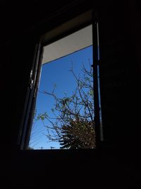 Low angle view of building against clear blue sky seen through window