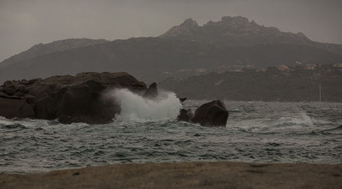 Sea waves splashing on rocks against sky