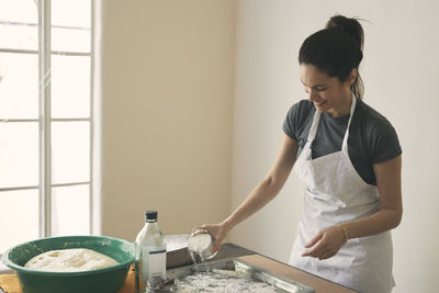 Smiling woman spreading flour on tray while preparing challah bread at home