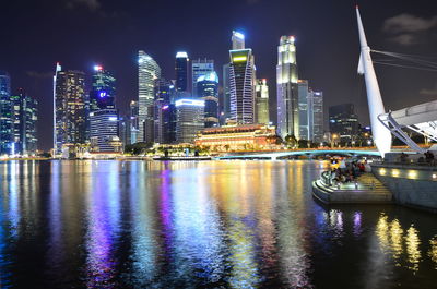 Illuminated city by river against sky at night