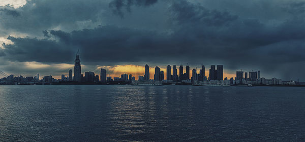 Sea by modern buildings against sky in city