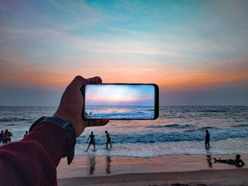 Man photographing at beach against sky during sunset