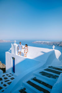 People at swimming pool by sea against clear blue sky