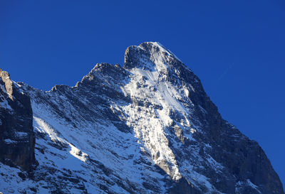 Low angle view of snowcapped mountains against clear blue sky