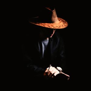 Midsection of man holding hat against black background