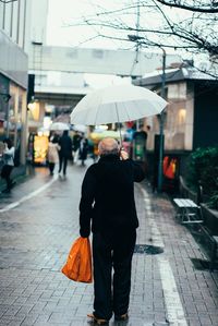 Rear view of senior man holding umbrella while walking on footpath
