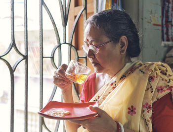 A simple looking indian housewife drinking her morning cup of tea, sitting beside window.