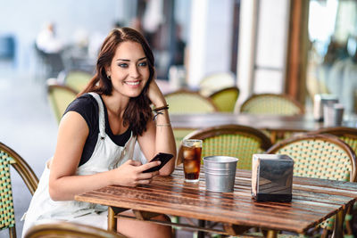 Portrait of smiling young woman using smart phone in cafe