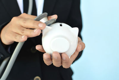 Midsection of doctor holding stethoscope and piggy bank while standing against blue background