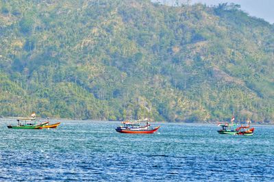 Boats sailing in sea against mountains