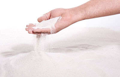 Cropped hand of man spilling sand against white background