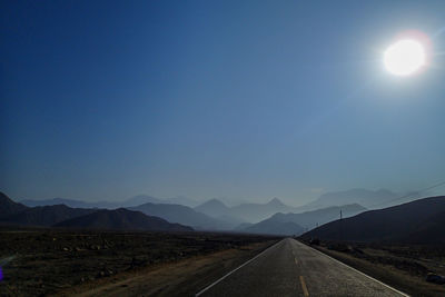 Road leading towards mountains against blue sky