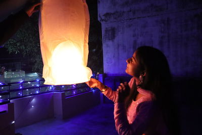 Side view of young woman holding illuminated lamp at night