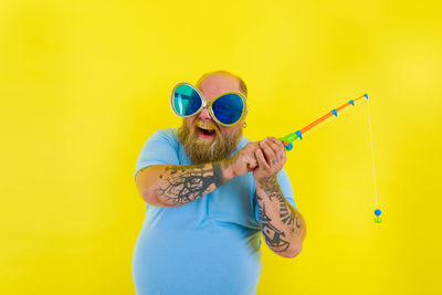 Portrait of man wearing sunglasses standing against yellow background