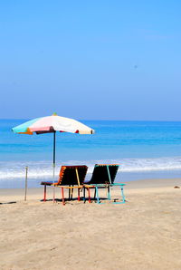 Seats on calm beach against blue sky