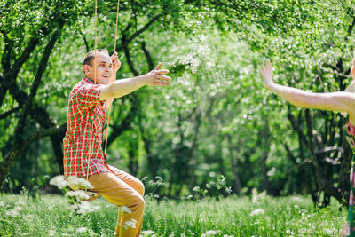 Happy man gesturing towards girlfriend while sitting on swing